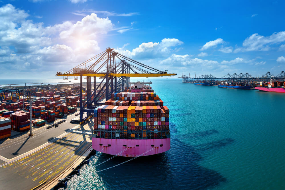 Ein großer Portalkran belädt ein Containerschiff im Hafen von Grünstadt; die Abwicklung erfolgt durch die Spedition.